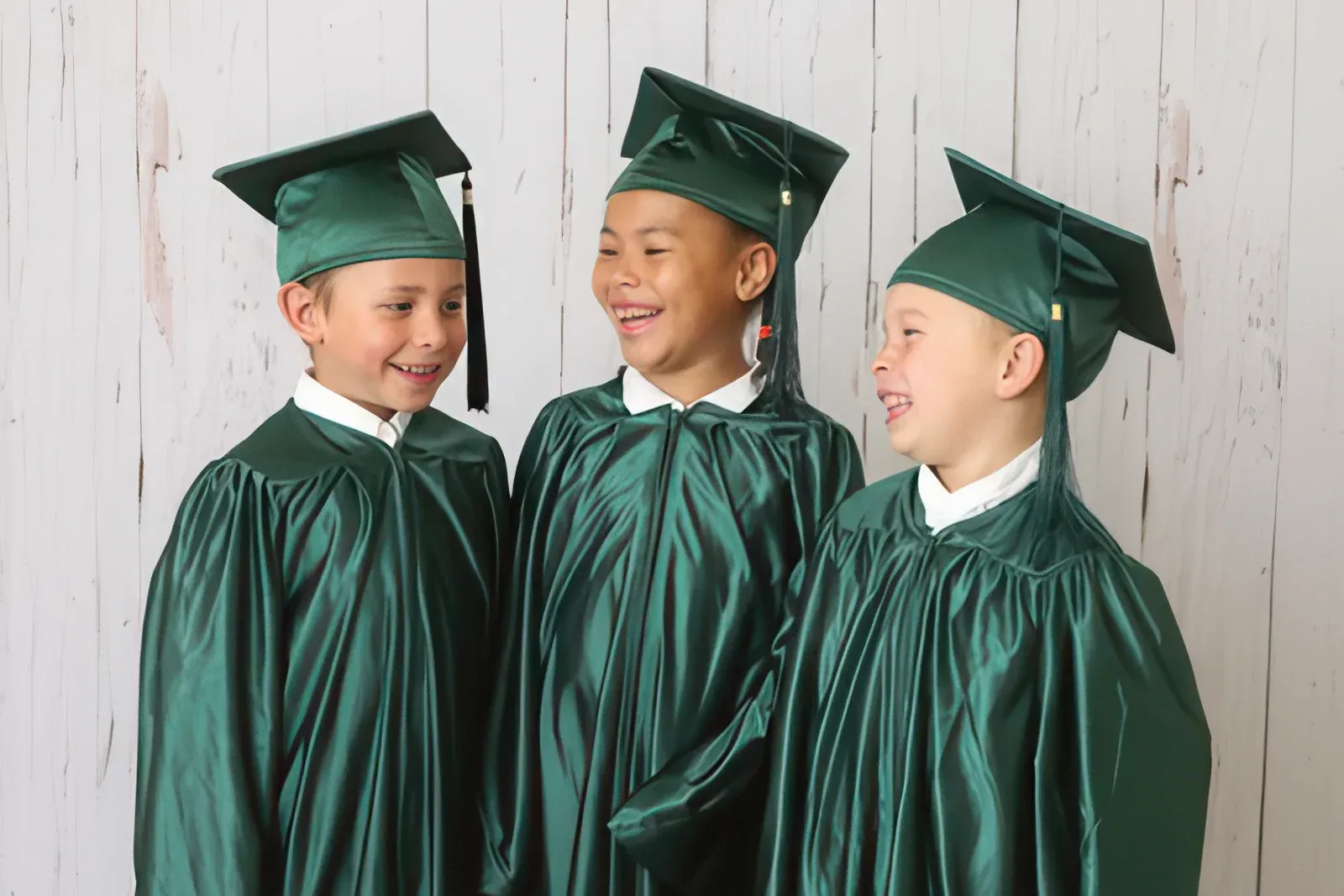 Three children in graduation caps and gowns, laughing together